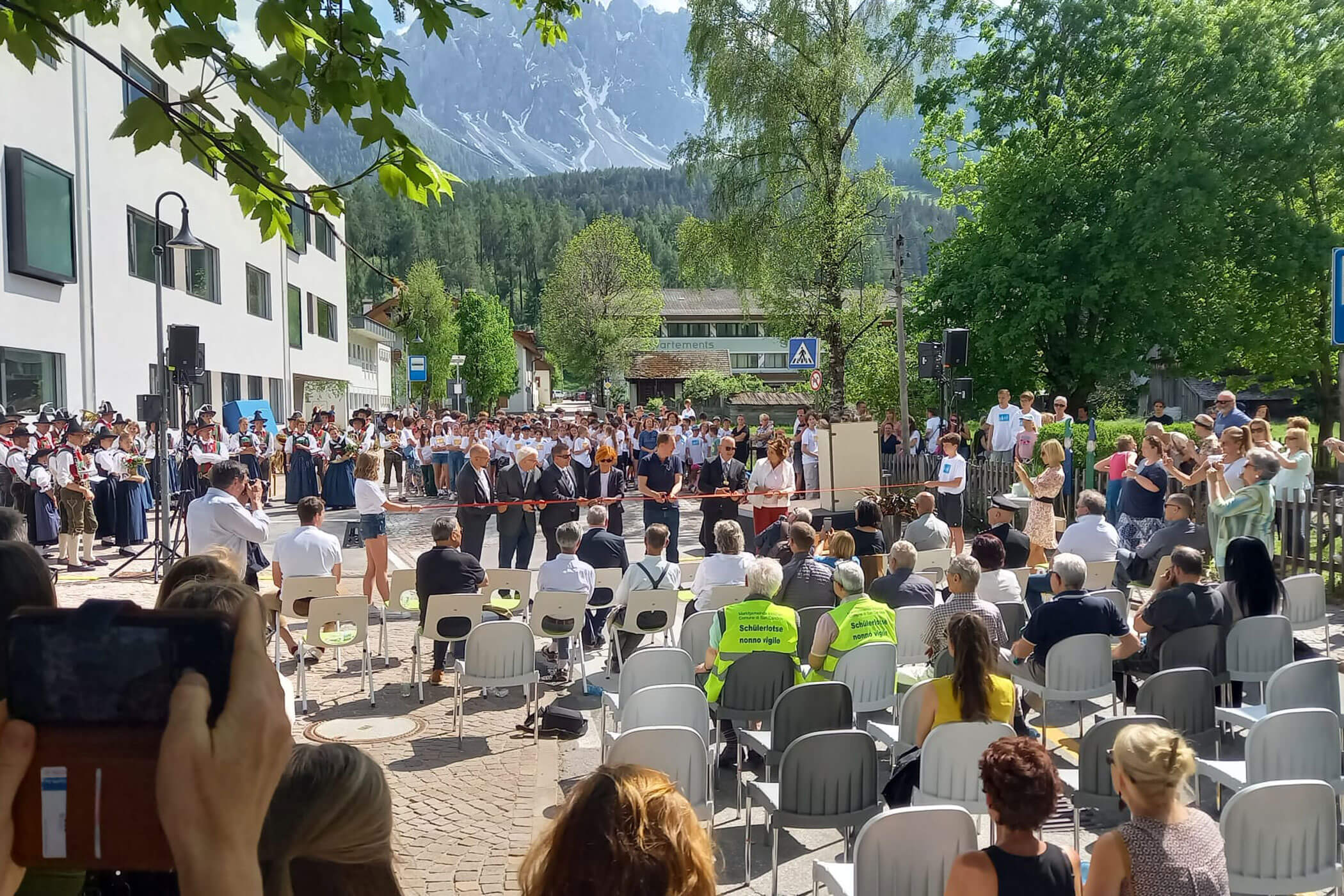 Eine große Veranstaltung im Freien mit Musikern und Publikum, vor der Kulisse von Bäumen und Bergen an einem sonnigen Tag. - HJPA Pro