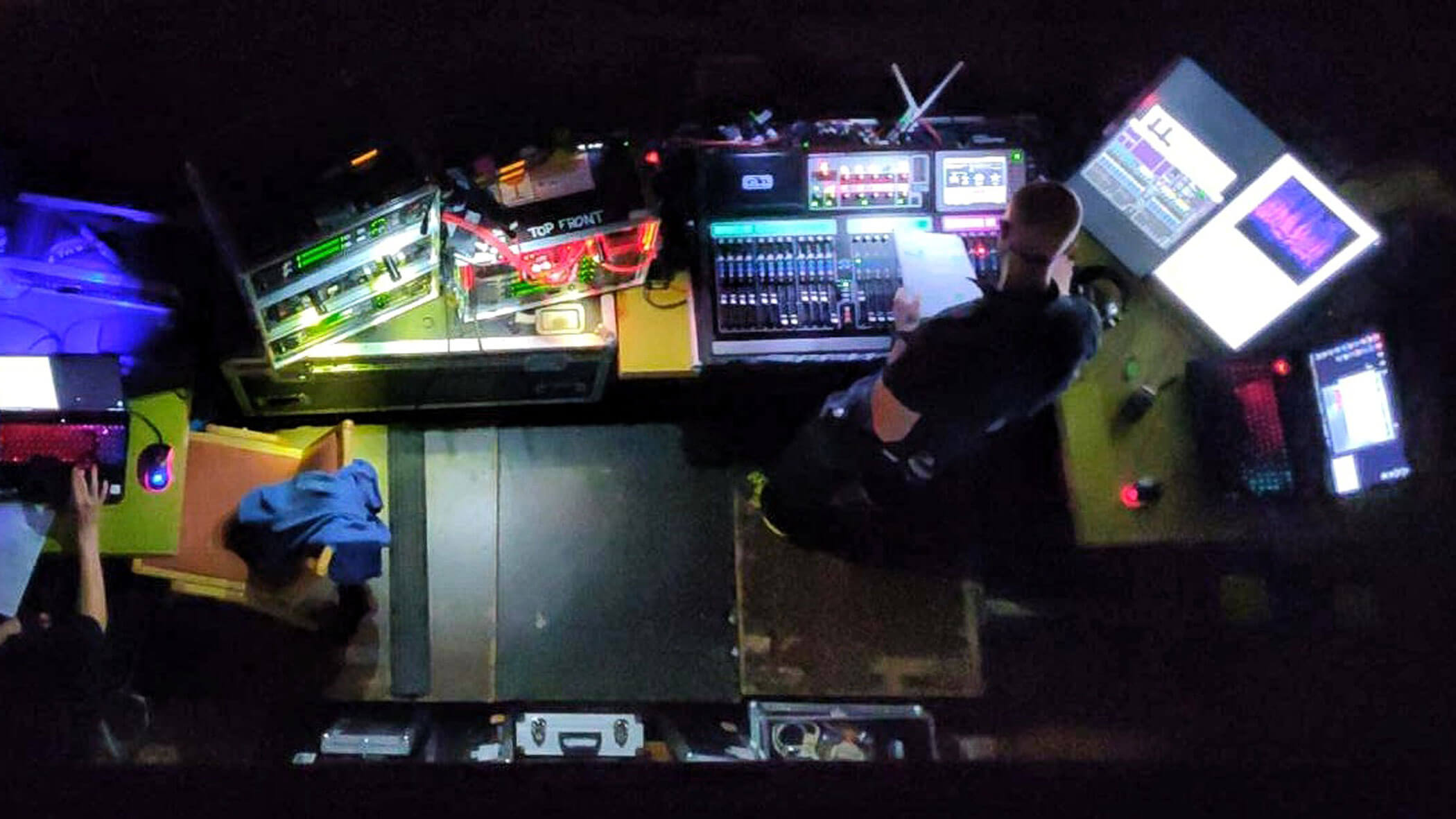 Draufsicht auf eine Person, die an einem Kontrollpult mit mehreren Bildschirmen Ton- und Lichttechnik bedient. - HJPA Pro