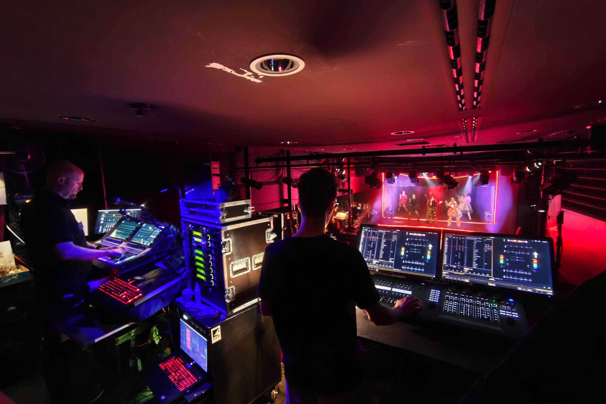 Das Backstage-Team bedient bei einem Live-Konzert die Licht- und Tonpulte, während die Bühne und die Künstler in bunten Lichtern erstrahlen. - HJPA Pro